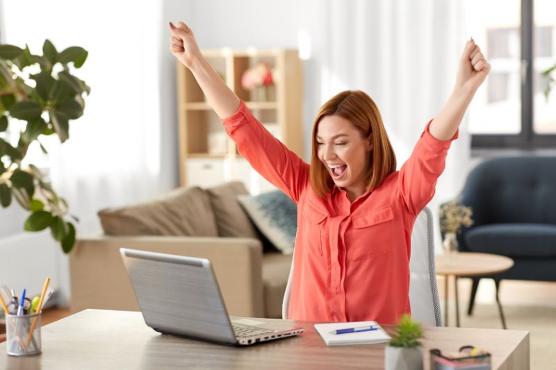 A woman celebrates with raised arms while sitting at a desk with a laptop where SPF, DKIM, DMARC was successfully implemented.