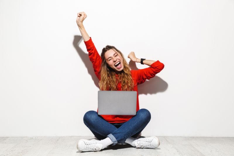 A woman with a laptop on her lap, raising her arms in celebration, having just cracked the code to effective B2B email marketing.