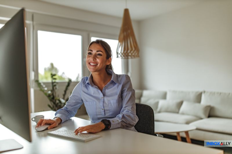 A woman is smiling while analyzing cold email open rates on her desktop computer