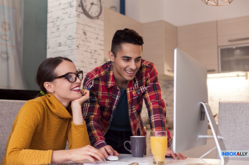 Two people in a modern kitchen discuss cold email open rates as they gaze at the computer screen. 