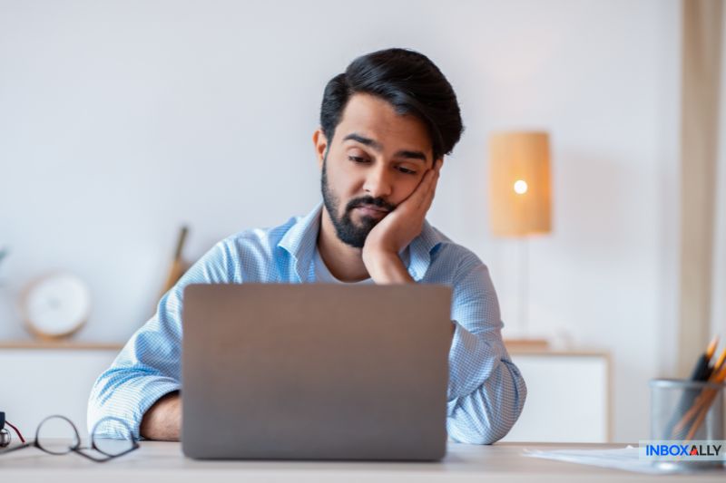 A person pondering whether cold emailing works, gazes thoughtfully at a laptop screen, chin resting on their hand. 