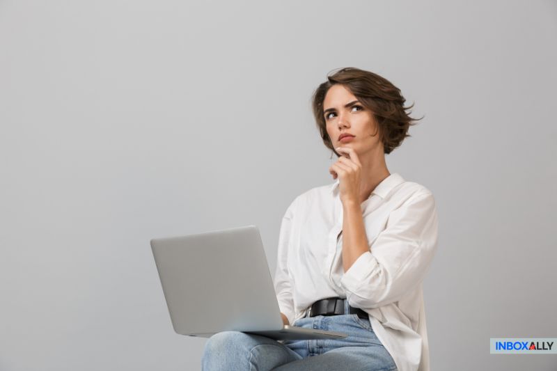 A lady sits on a stool, clutching a laptop and pondering, perhaps contemplating the question: Does cold emailing work?