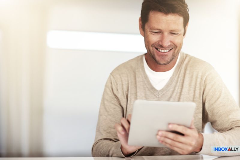 A man smiles confidently while using a tablet, perhaps pondering the age-old question: Does cold emailing work?