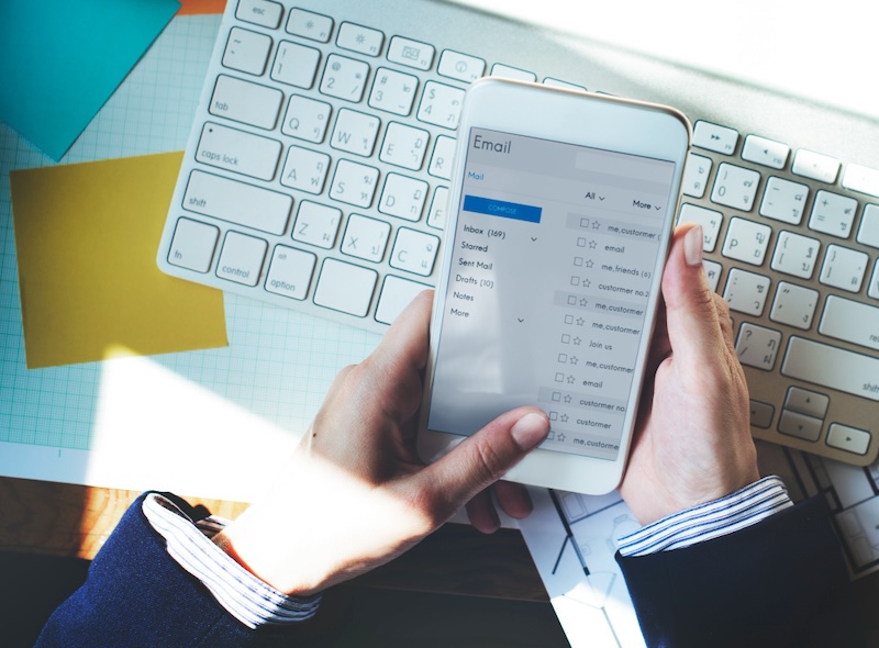 Person holding a smartphone displaying an email inbox. The setup suggests a thoughtful approach to follow-up emails by balancing email frequency and ensuring proper follow up etiquette.