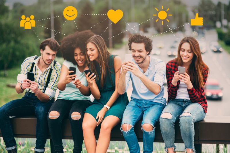 Group of five young adults sitting together and sharing content and smiling at their smartphones as they discuss cold email strategies.