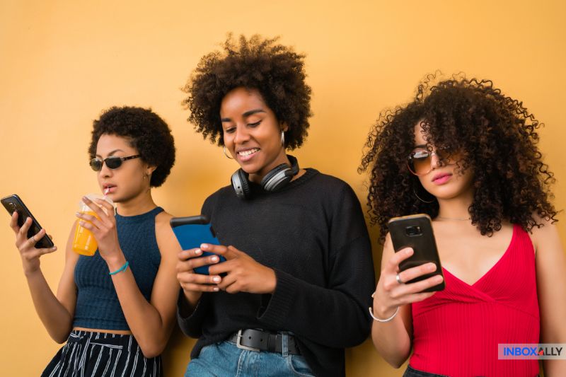 Three people stand against a Wall, using smartphones crafting cold emails that get opened.