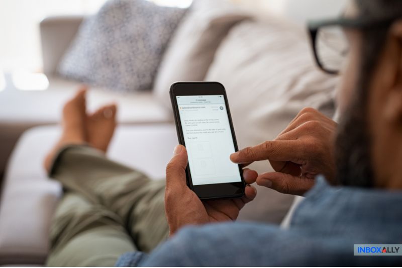 Relaxing on the sofa, the person scrolls effortlessly through their smartphone, eyes scanning a website dedicated to crafting cold emails that get opened.