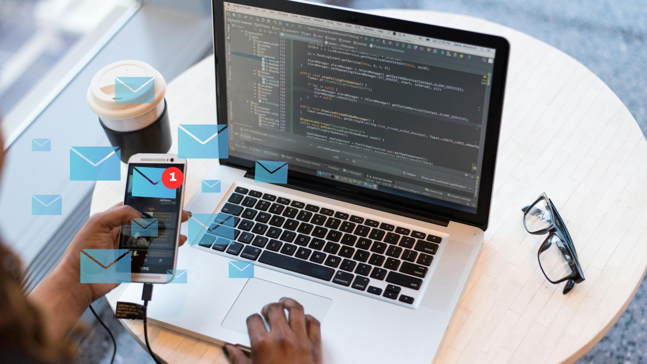 Uma pessoa usa um smartphone e um laptop em uma mesa, ambos os dispositivos exibindo código de desenvolvimento de software e ícones de notificação, incluindo aqueles para uma campanha de e-mail.  