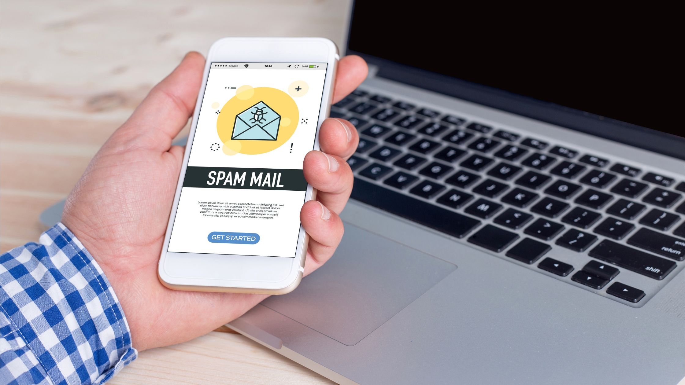 A person holds a smartphone displaying a spam mail notification while sitting at a desk with an open laptop, attempting to bypass spam filters.