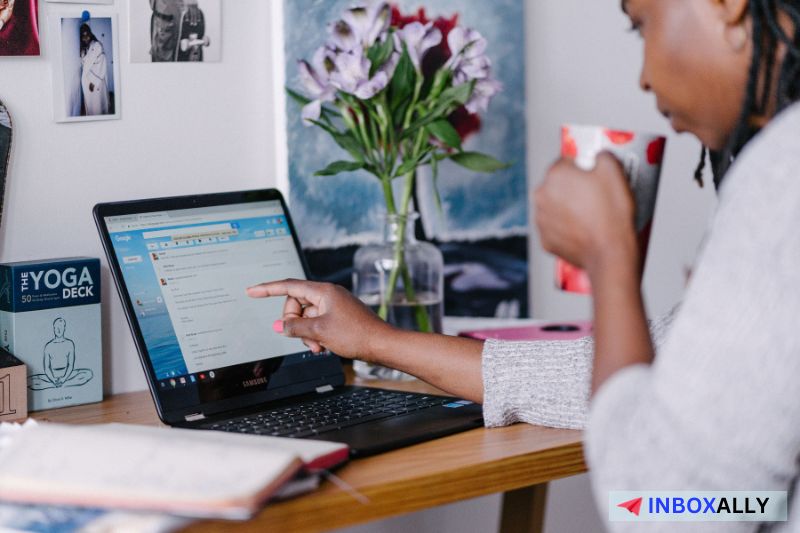 Pessoa sentada em uma mesa, segurando uma caneca e apontando para a tela de um laptop com uma caixa de entrada de e-mail aberta enquanto pesquisa como corrigir problemas de entrega de e-mail.