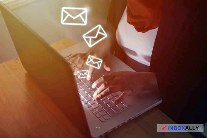 A person typing on a laptop, with illustrated email icons floating above the keyboard, prepares for a mass email campaign. 