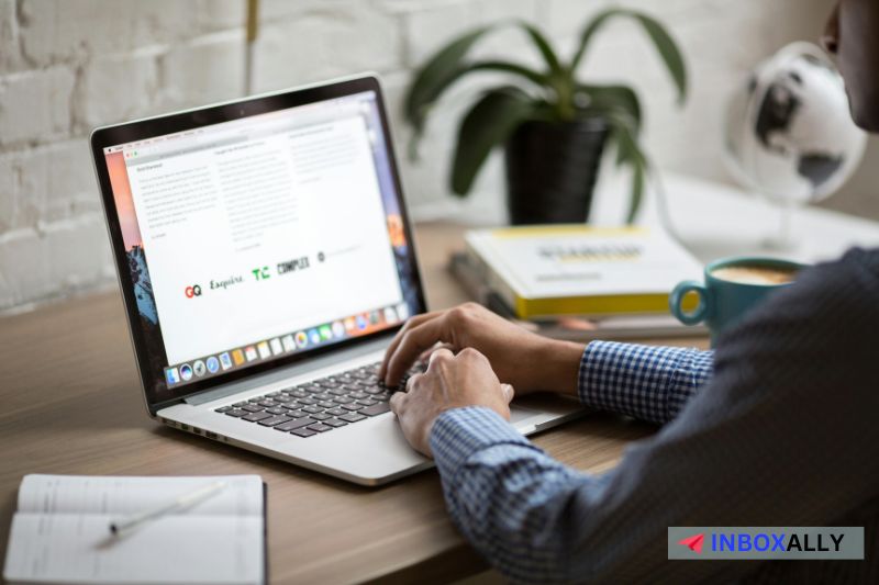 Person typing on a laptop at a wooden desk with a notebook, crafting a mass email for 2024 campaigns.