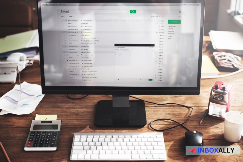 A computer monitor displays an email inbox on a cluttered desk with a keyboard, The email format shifts between plain text emails and rich HTML emails as it previews the best format for 2024.