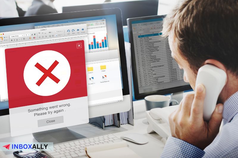 A man on the phone looks at a computer screen displaying an error message with a red cross, pondering the ominous "550 Permanent Failure" email error.