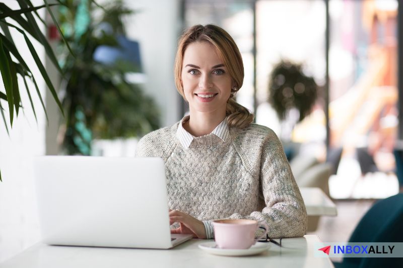 A person with a laptop sits at a table as they browse through a simple guide on one-click unsubscribe options. Lush plants and blurred background elements create a serene atmosphere.