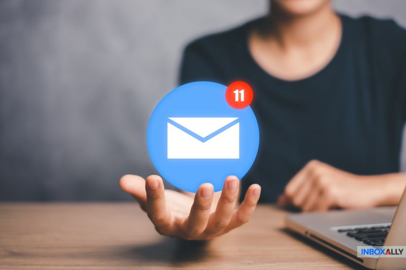 Uma pessoa segura um ícone de e-mail digital com a notificação número 11, sentada ao lado de um laptop, pensando em sua estratégia de marketing por e-mail.