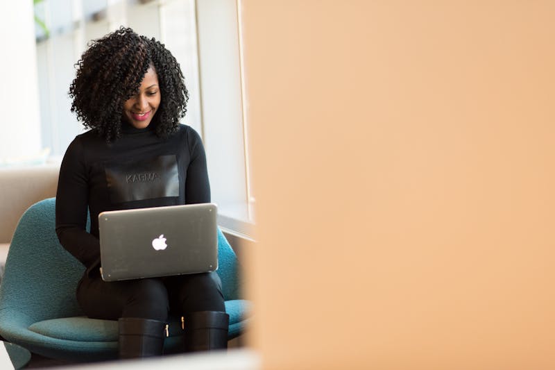 Person with curly hair sitting on a chair, using a laptop to manage their crowded inbox, pondering the psychology of sender reputation to build trust in communication.