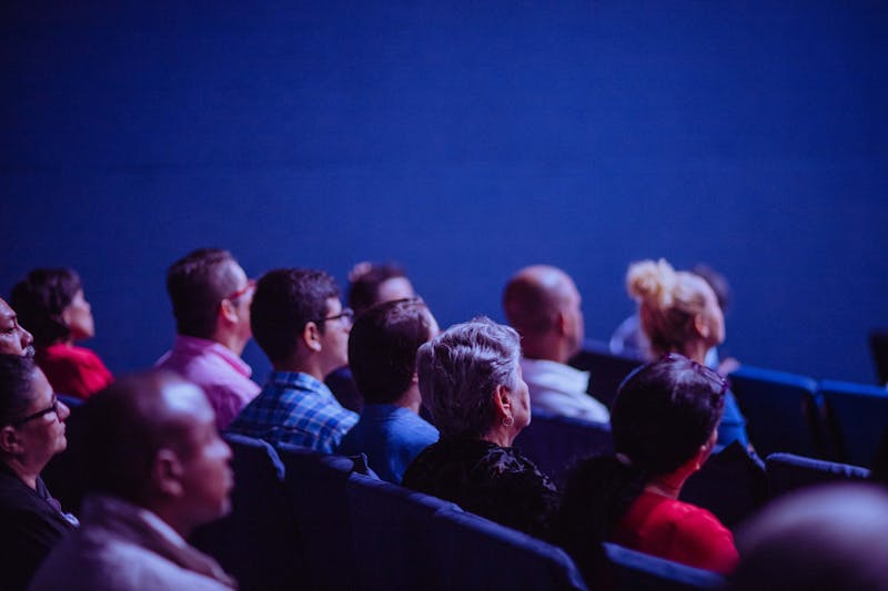 Audience members seated in a dimly lit theater, captivated by the performance, as if building trust with the actors on stage.