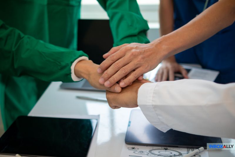 A group of people in medical attire stack their hands over a table with devices, symbolizing teamwork for better inbox placement.