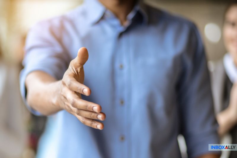 Pessoa de camisa azul estendendo a mão para um aperto de mão, incorporando o espírito de receber novos clientes de braços abertos.