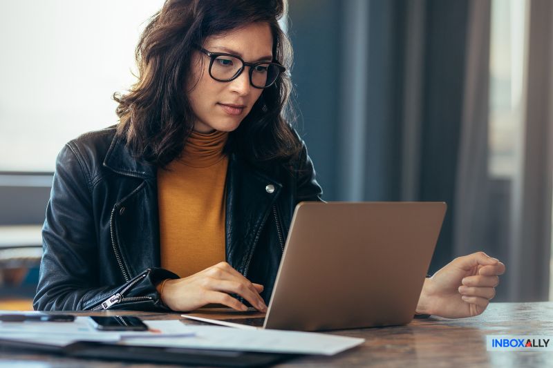 Uma mulher profissional de óculos usando um laptop para explorar o InboxAlly como uma alternativa de teste de e-mail para evitar filtros de spam.