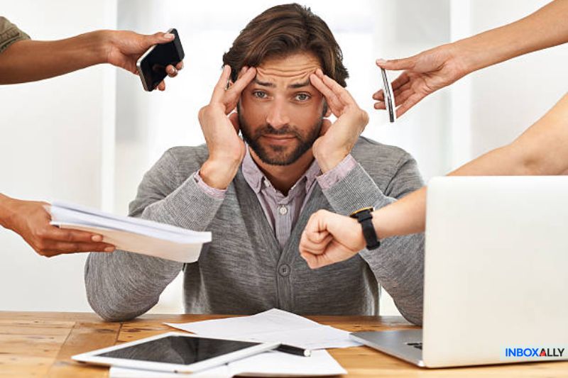 Stressed marketer surrounded by devices and documents, representing challenges in mastering the open rate formula for email campaigns